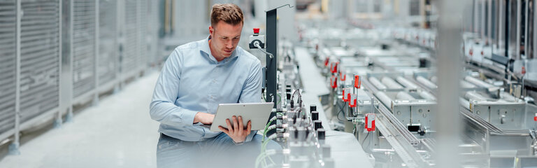 Engineer sitting at an assembly line with a laptop in his hand